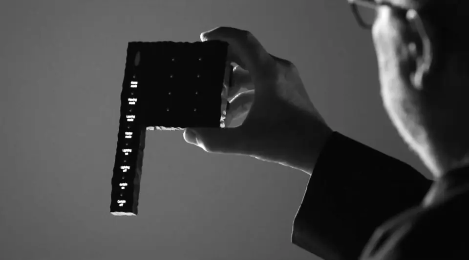 Hand holding a slim black Moorgen Philippe Starck control with a column of backlit buttons