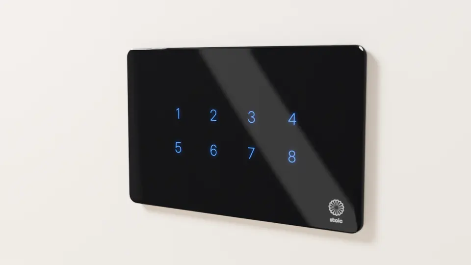 Stoic wide touch panel in glossy black glass with eight lit blue icon keys in two rows and the Stoic logo bottom-right, on a cream wall